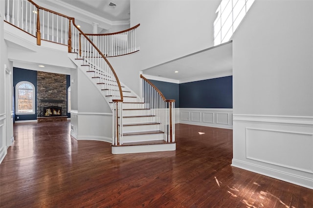 interior space featuring crown molding, a decorative wall, a towering ceiling, a stone fireplace, and wood finished floors