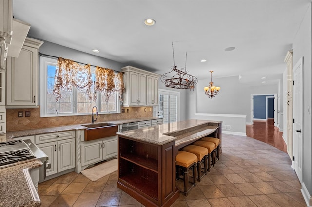 kitchen featuring light stone counters, a breakfast bar area, a sink, a kitchen island, and decorative backsplash