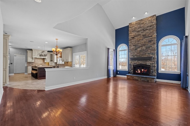 unfurnished living room with baseboards, wood finished floors, a fireplace, high vaulted ceiling, and a notable chandelier