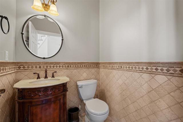 bathroom featuring wainscoting, toilet, a notable chandelier, vanity, and tile walls