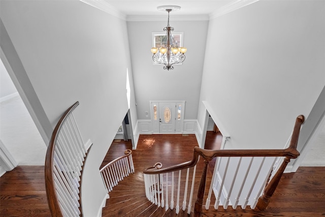 interior space featuring a wainscoted wall, wood finished floors, crown molding, a decorative wall, and a notable chandelier