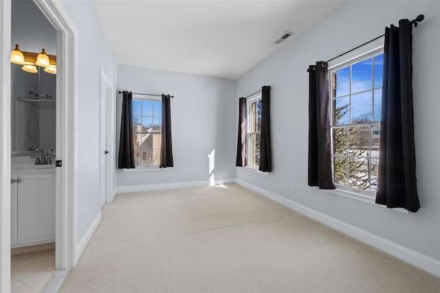 empty room featuring visible vents, a sink, light carpet, and baseboards