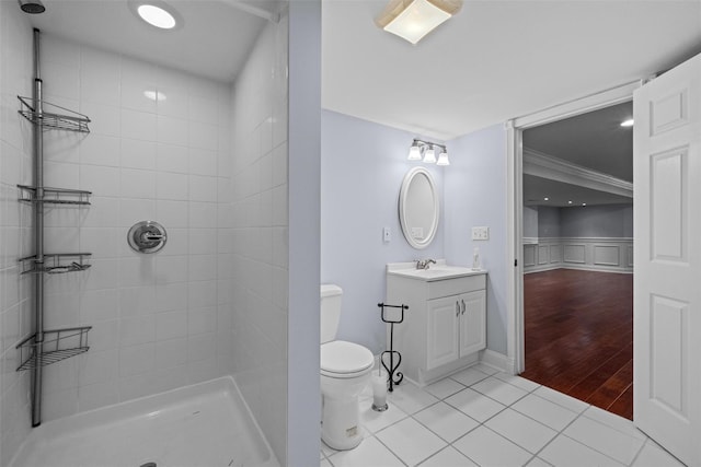 bathroom with toilet, ornamental molding, tile patterned floors, a tile shower, and vanity