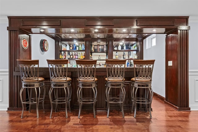 bar with crown molding, bar area, a decorative wall, and wood finished floors