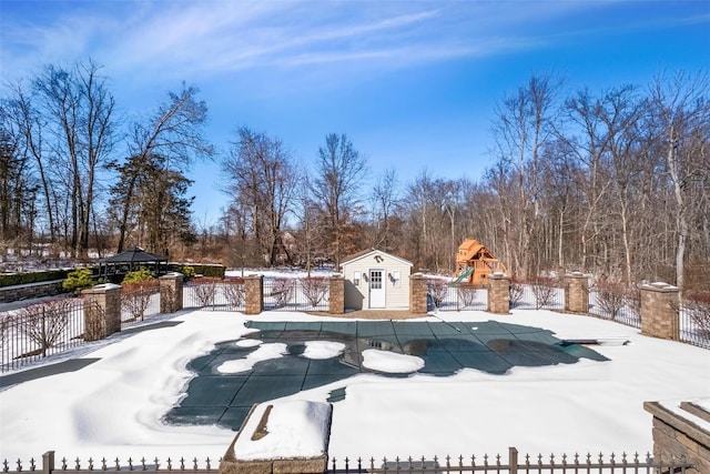 snow covered pool with an outbuilding, a playground, fence, and a fenced in pool