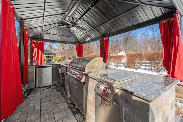 snow covered patio featuring area for grilling, a gazebo, an outdoor kitchen, and a ceiling fan