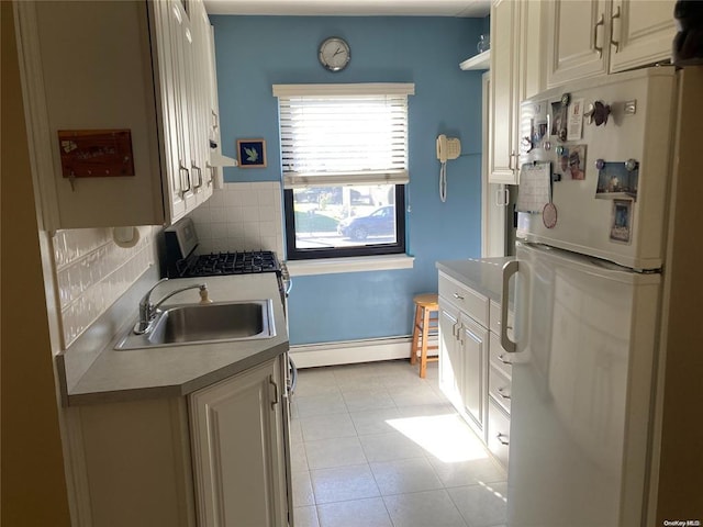 kitchen with tasteful backsplash, freestanding refrigerator, light countertops, a baseboard heating unit, and a sink