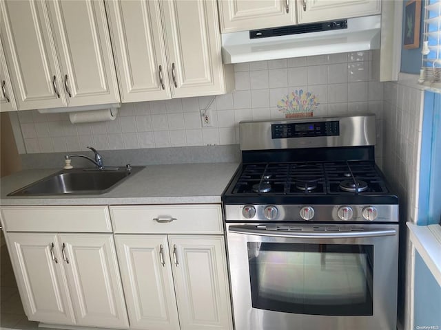 kitchen with stainless steel gas stove, under cabinet range hood, white cabinetry, and a sink