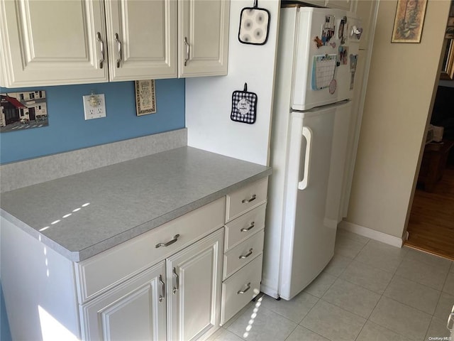 kitchen with light tile patterned floors, light countertops, freestanding refrigerator, white cabinetry, and baseboards