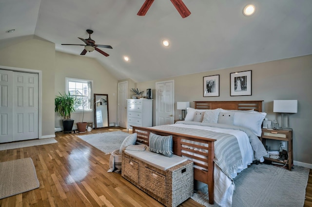 bedroom with ceiling fan, vaulted ceiling, wood finished floors, baseboards, and multiple closets