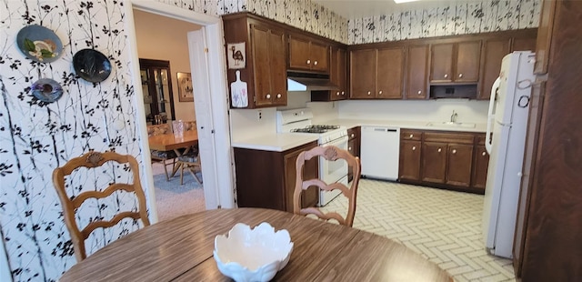 kitchen with white appliances, wallpapered walls, light countertops, under cabinet range hood, and a sink