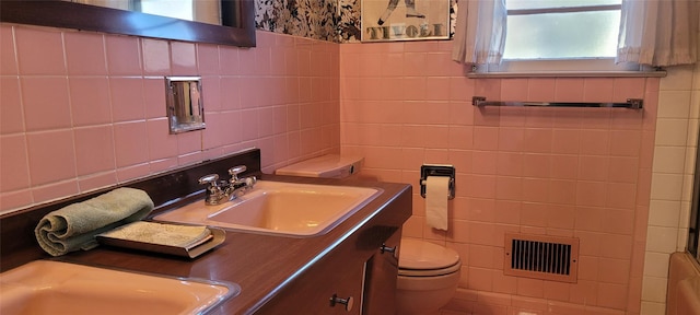 full bathroom featuring double vanity, visible vents, toilet, a sink, and tile walls