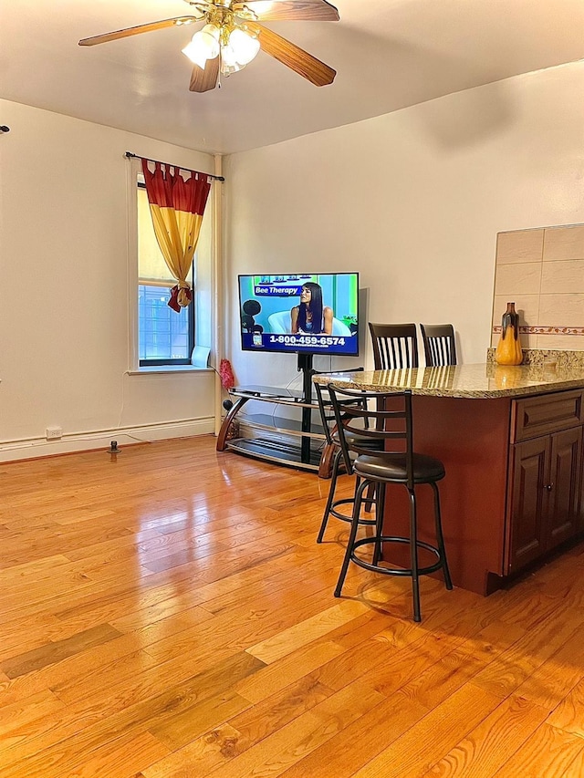 bar featuring baseboards, backsplash, a ceiling fan, and light wood-style floors