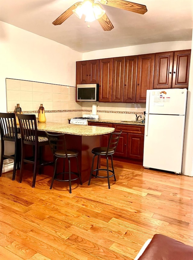 kitchen with stove, a kitchen breakfast bar, light wood-type flooring, freestanding refrigerator, and stainless steel microwave