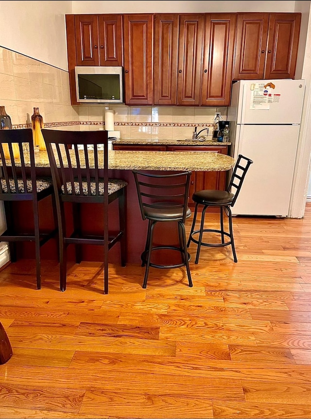 kitchen with tasteful backsplash, light wood-style flooring, stainless steel microwave, a breakfast bar, and freestanding refrigerator