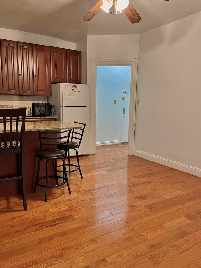 kitchen featuring freestanding refrigerator, ceiling fan, a kitchen breakfast bar, light wood-type flooring, and baseboards