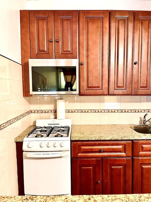 kitchen featuring stainless steel microwave, a sink, light stone countertops, and white range with gas stovetop