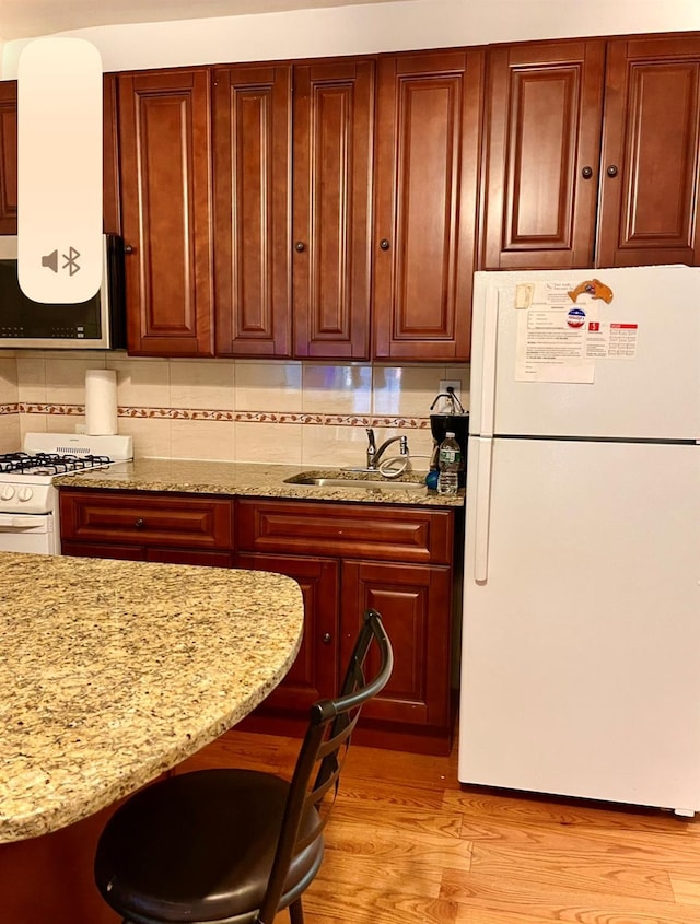 kitchen with light stone counters, backsplash, light wood-style floors, a sink, and white appliances