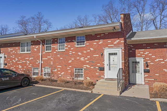 exterior space with uncovered parking, brick siding, and a chimney