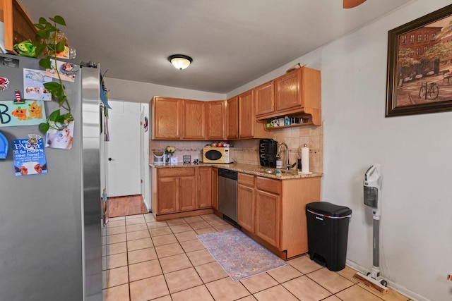 kitchen featuring appliances with stainless steel finishes, backsplash, light stone countertops, a sink, and light tile patterned flooring