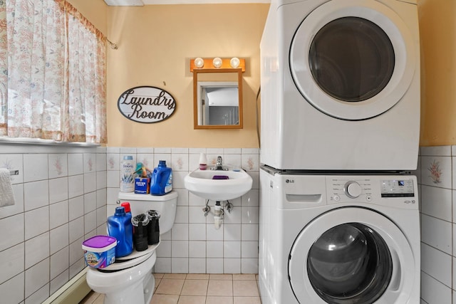 washroom with tile walls, stacked washer / drying machine, a baseboard heating unit, laundry area, and tile patterned floors