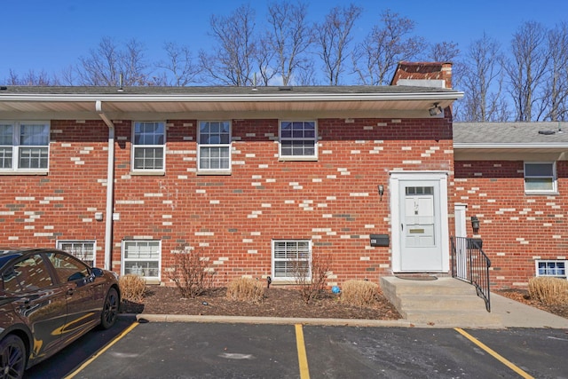 view of front of home featuring uncovered parking, brick siding, and a chimney