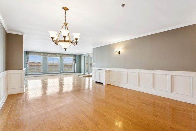 unfurnished room featuring a decorative wall, wainscoting, light wood-type flooring, an inviting chandelier, and crown molding