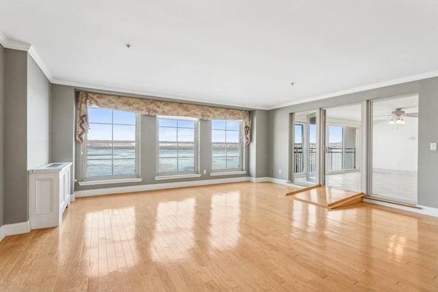 unfurnished room featuring light wood-style floors, a water view, crown molding, and baseboards