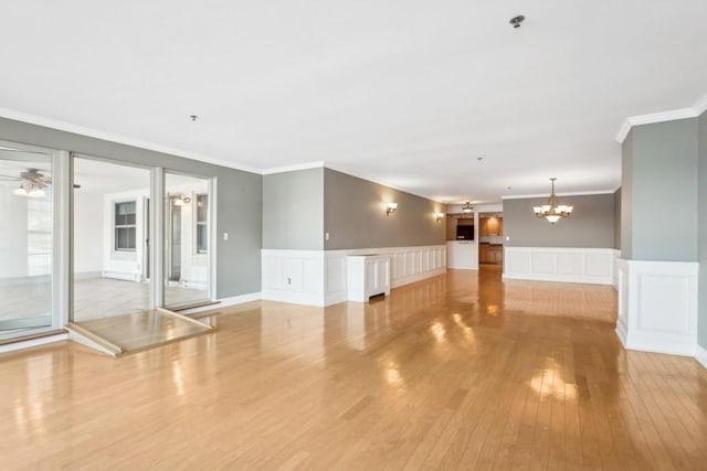 spare room featuring ceiling fan with notable chandelier, crown molding, wainscoting, and light wood-style floors