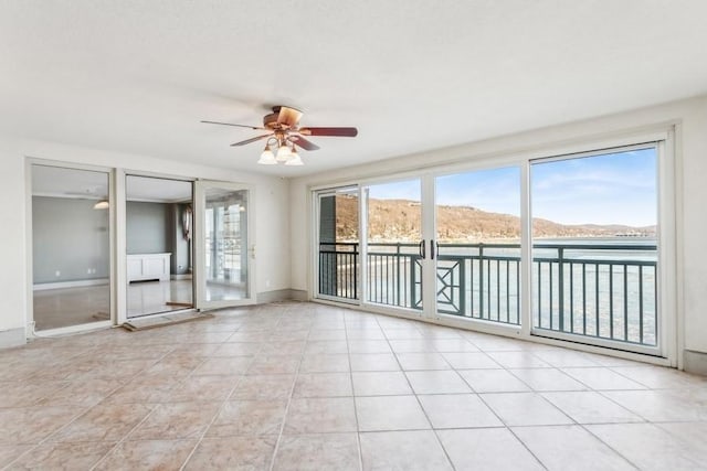 unfurnished room featuring ceiling fan, light tile patterned floors, plenty of natural light, and a water and mountain view