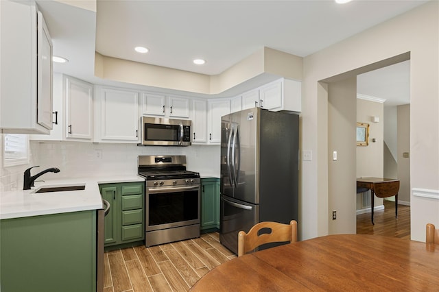 kitchen featuring light wood finished floors, tasteful backsplash, green cabinets, appliances with stainless steel finishes, and a sink