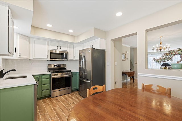 kitchen with light wood-style flooring, a sink, white cabinets, green cabinets, and appliances with stainless steel finishes