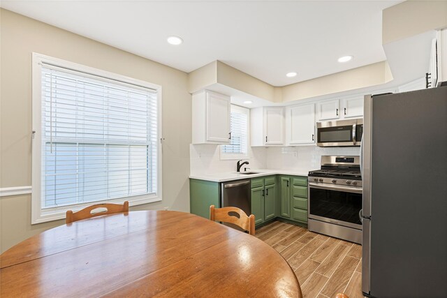 kitchen with stainless steel appliances, wood finish floors, white cabinetry, green cabinets, and a sink