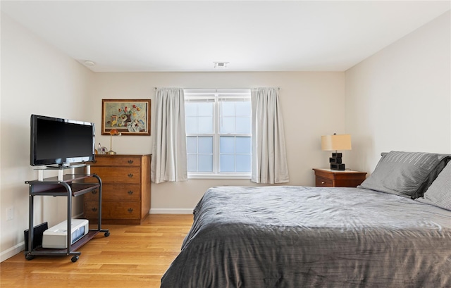 bedroom with baseboards, visible vents, and wood finished floors