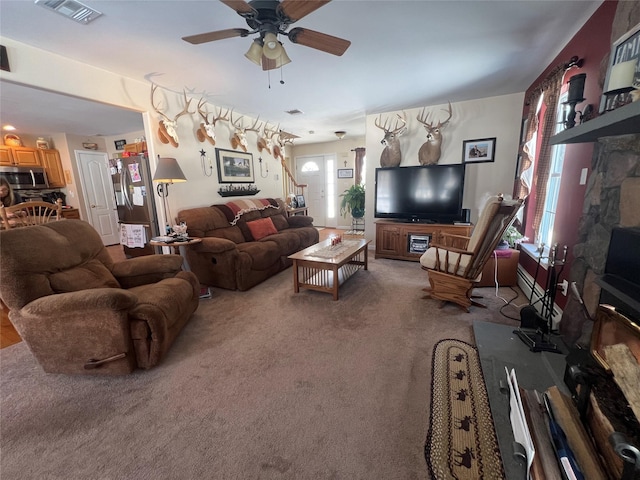 carpeted living area featuring visible vents, ceiling fan, and stairway