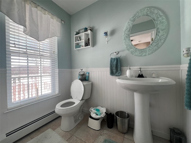 bathroom with a baseboard heating unit, tile patterned flooring, a wainscoted wall, and toilet