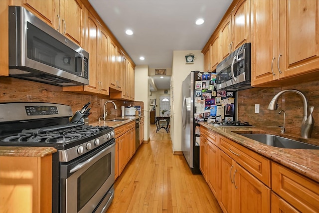 kitchen with light stone countertops, light wood-style flooring, appliances with stainless steel finishes, and a sink