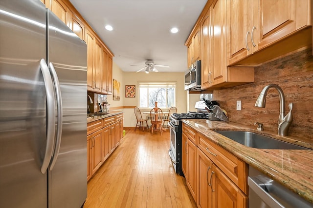 kitchen with light stone counters, a sink, light wood-style floors, appliances with stainless steel finishes, and decorative backsplash