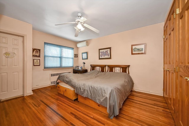 bedroom with radiator, light wood-style floors, baseboards, and a wall mounted air conditioner