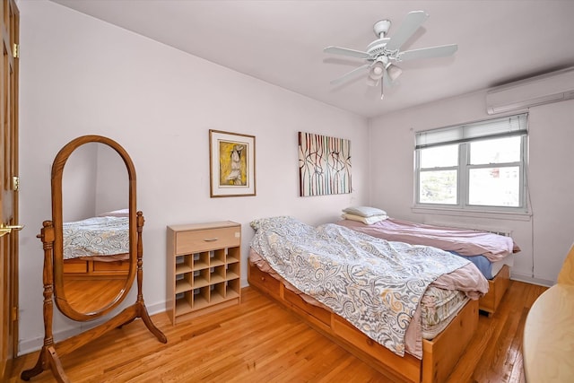 bedroom with a ceiling fan, light wood-type flooring, a wall mounted air conditioner, and baseboards