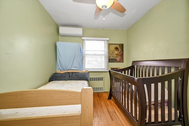 bedroom with radiator, ceiling fan, wood finished floors, and a wall mounted AC