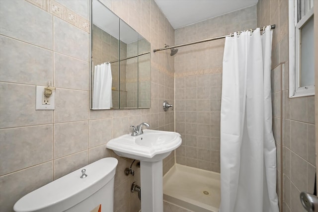 bathroom with toilet, a stall shower, a sink, and tile walls