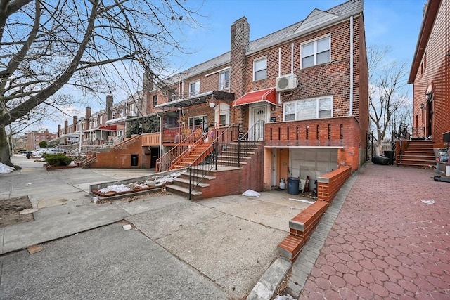 exterior space with driveway, brick siding, a chimney, stairway, and a wall mounted AC