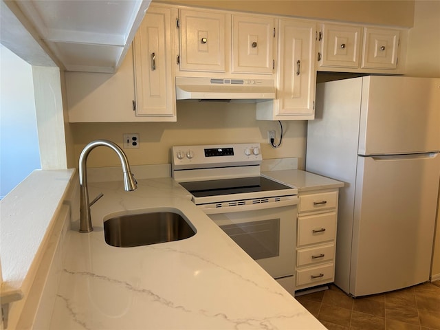 kitchen with white appliances, light stone counters, under cabinet range hood, dark tile patterned floors, and a sink