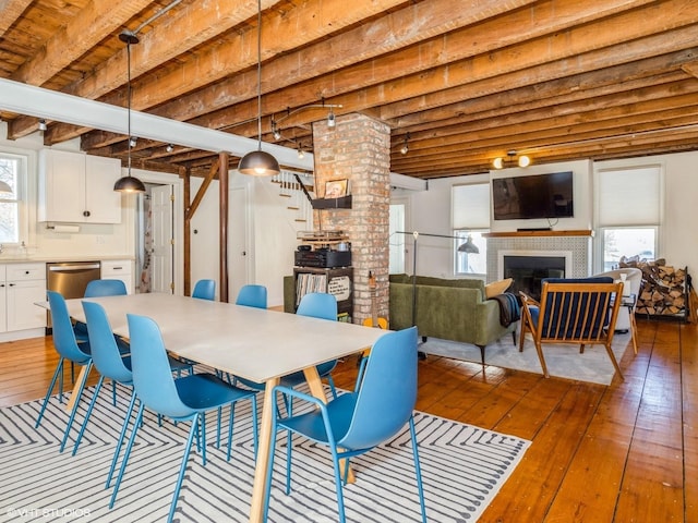 dining space with a fireplace, stairway, beamed ceiling, and hardwood / wood-style flooring