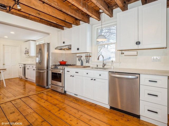 kitchen featuring under cabinet range hood, a sink, light countertops, appliances with stainless steel finishes, and beamed ceiling