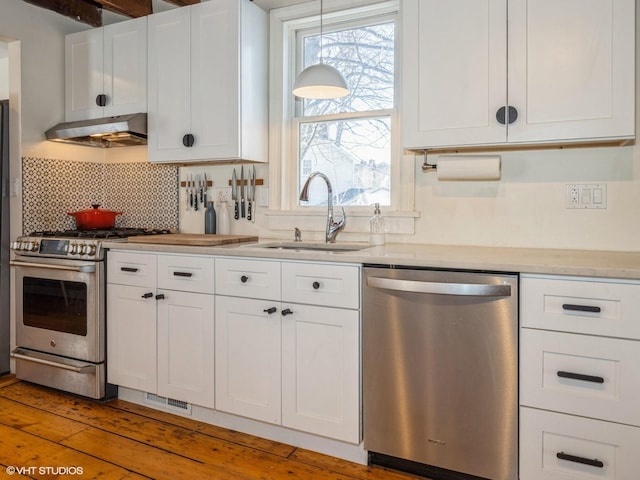 kitchen with tasteful backsplash, stainless steel appliances, under cabinet range hood, white cabinetry, and a sink