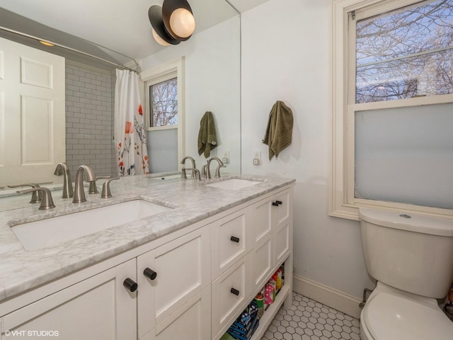 bathroom featuring double vanity, a sink, toilet, and baseboards