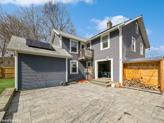 rear view of property featuring a balcony, fence, roof mounted solar panels, a chimney, and a patio area