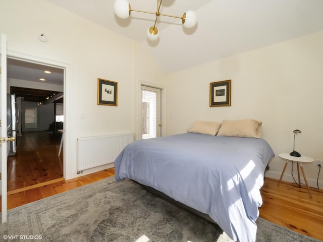 bedroom featuring lofted ceiling, wood finished floors, baseboards, freestanding refrigerator, and radiator heating unit